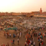 Vista panorámica de la Plaza Jemaa el-Fna en Marrakech, con multitudes disfrutando de la diversidad cultural y el entretenimiento callejero.