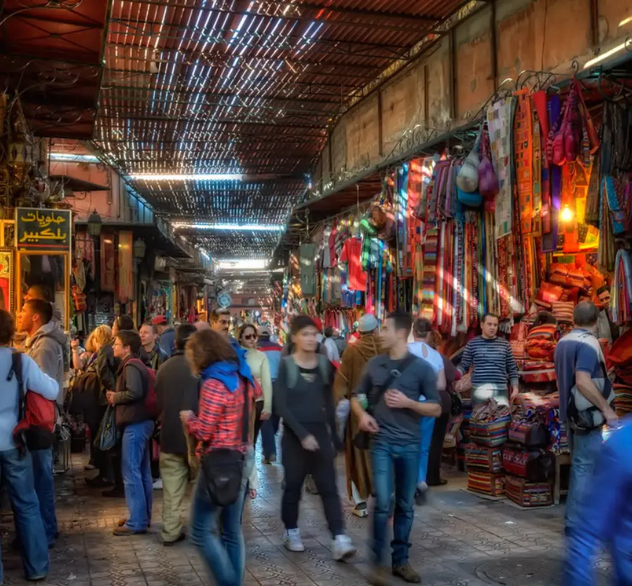 Vista colorida y bulliciosa de los Zocos de Marrakech, con vendedores y clientes explorando las tiendas y puestos